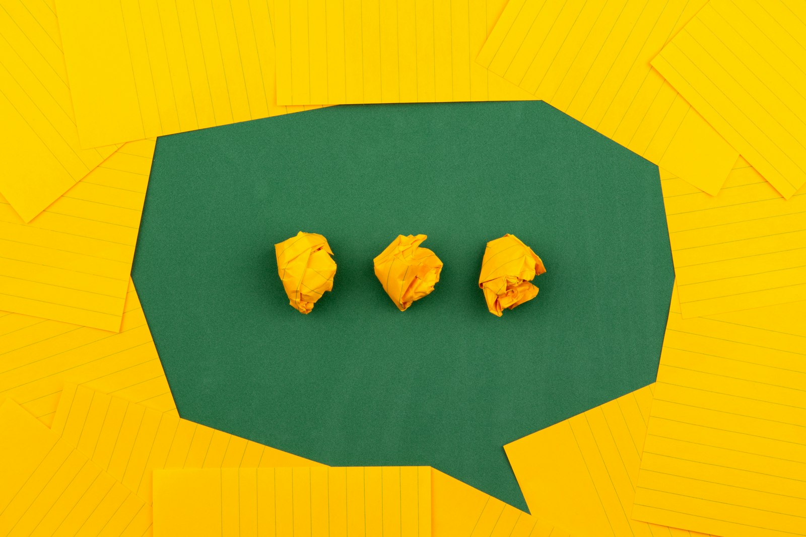 A speech bubble cut from paper holding three crumpled paper balls like a typing indicator
